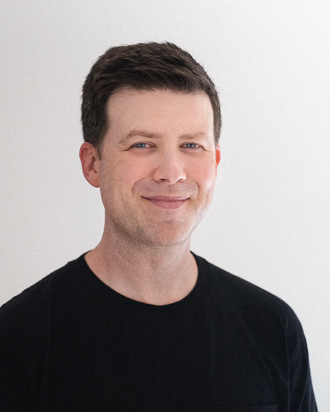 Portrait photo of designer Greg Gunn wearing a black shirt looking at camera.
